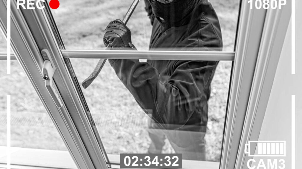 Burglar breaking in to home through window with crowbar