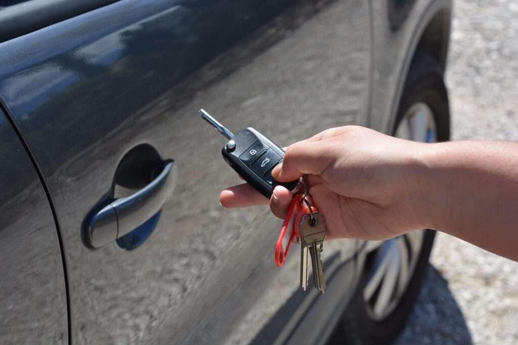 Car key in hand, next to vehicle. Remote keyless entry system and ignition key