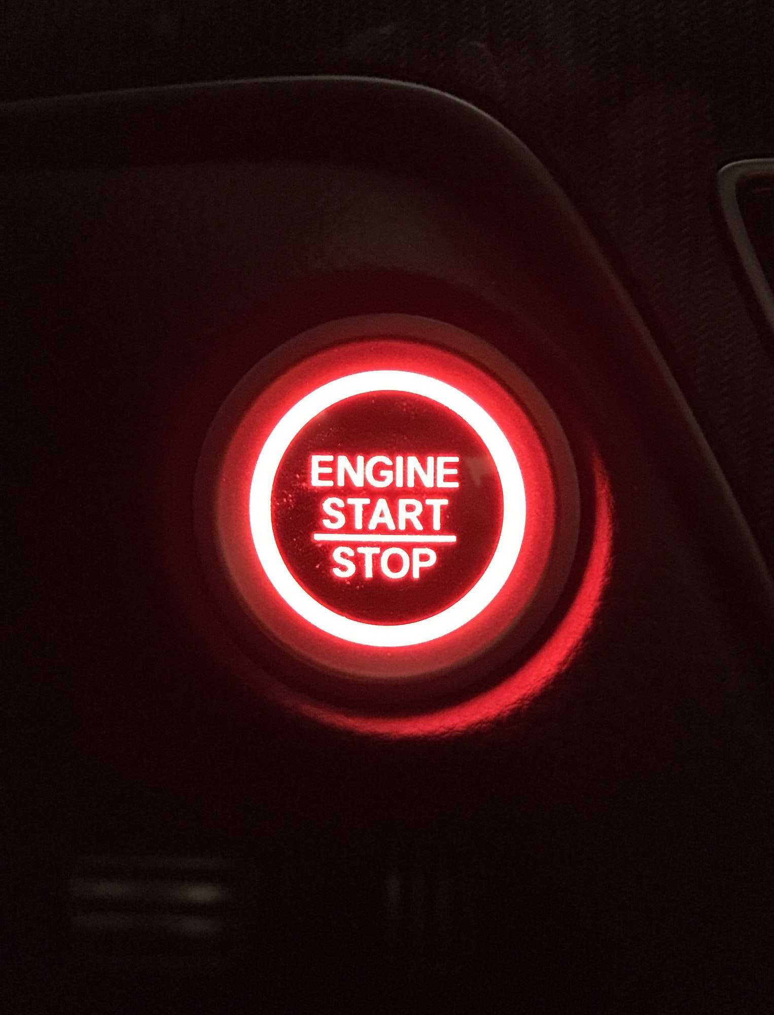 Modern automobile illuminated engine start stop ignition button in red